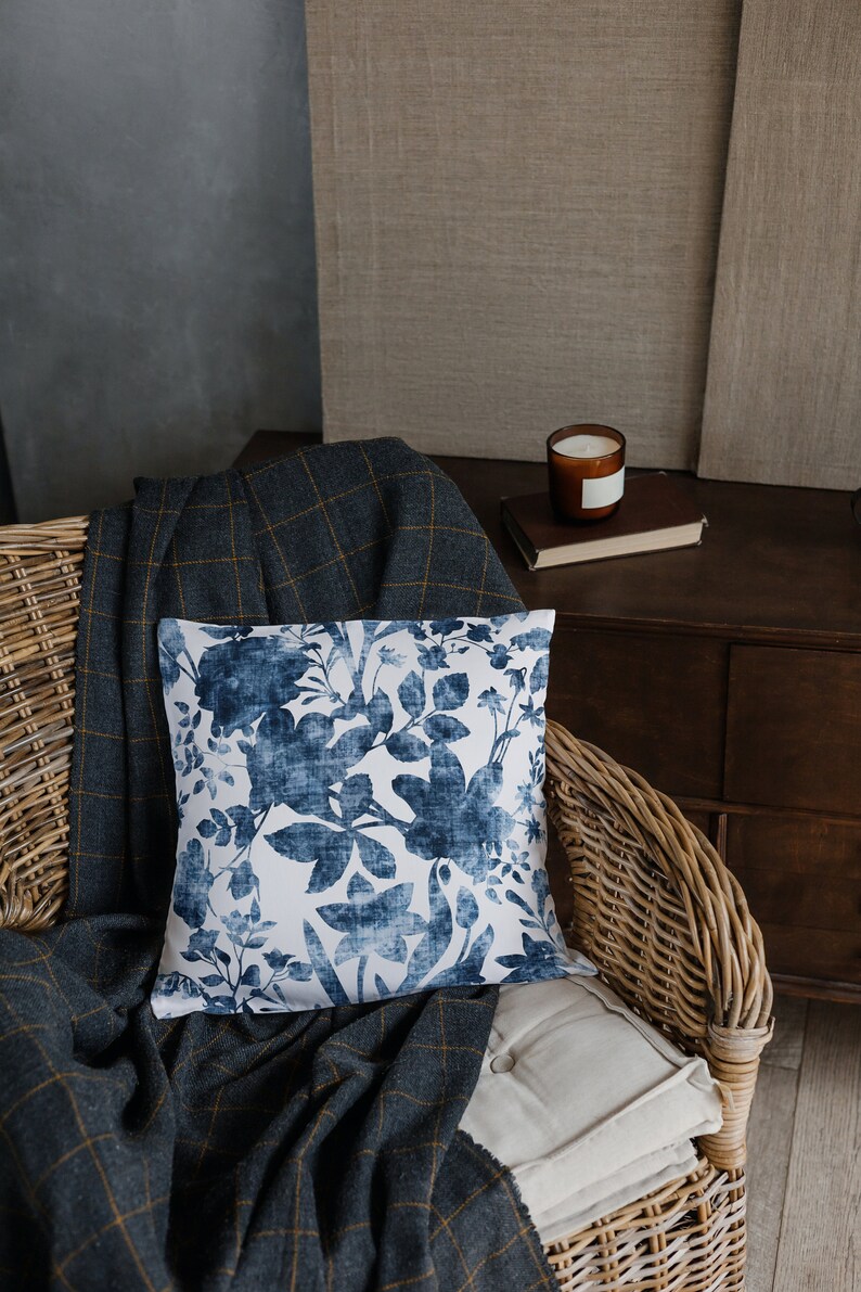 May include: A wicker chair with a blue and white floral patterned cushion, a grey and yellow checked throw blanket, and a white cushion.