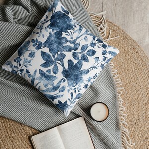 May include: A blue and white floral patterned cushion on a grey and white striped throw with a book and a candle on a jute rug.