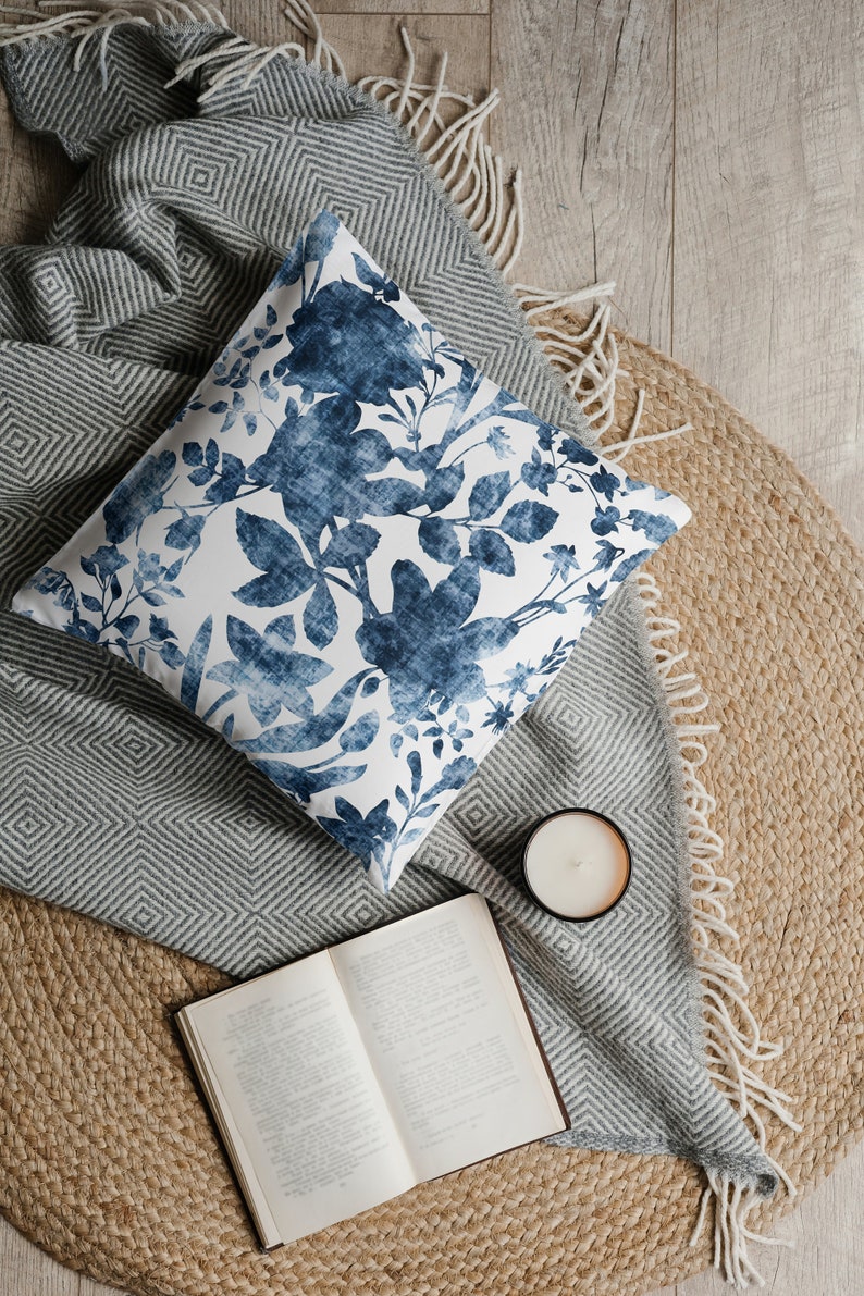 May include: A blue and white floral patterned cushion on a grey and white striped throw with a book and a candle on a jute rug.