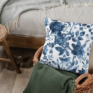 May include: A blue and white floral patterned cushion in a wicker basket with a green throw blanket.