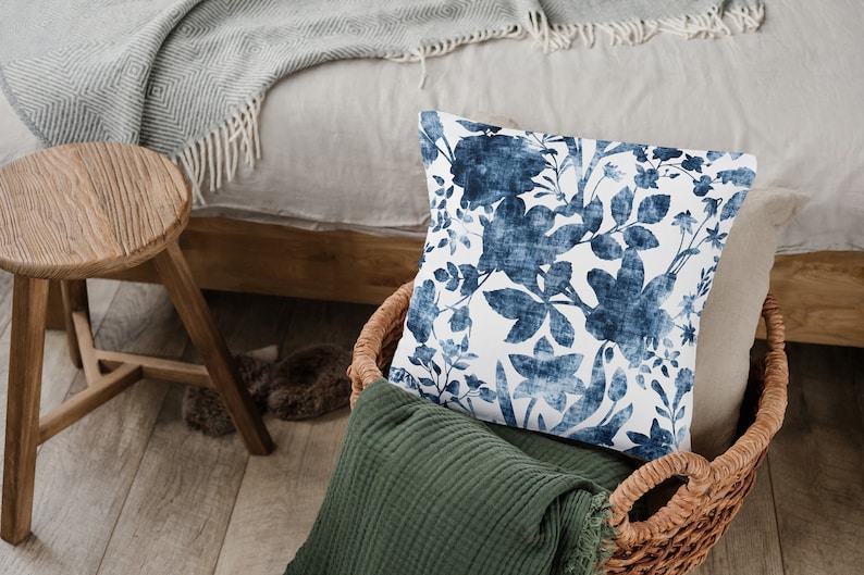 May include: A blue and white floral patterned cushion in a wicker basket with a green throw blanket.