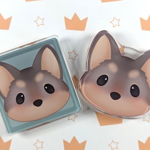 May include: Two clear acrylic pins featuring a cartoon wolf head. One pin is square with a light blue background, the other is shaped like the wolf's head. The wolf has brown and gray fur, large black eyes, and a pink nose.