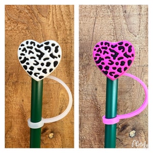 May include: Two green sticks with white and pink heart-shaped toppers featuring a black and white leopard print design. Each stick has a white or pink loop attached.