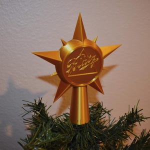 May include: A gold star-shaped Christmas tree topper with a circular design featuring the text "Merry" in a stylized font.