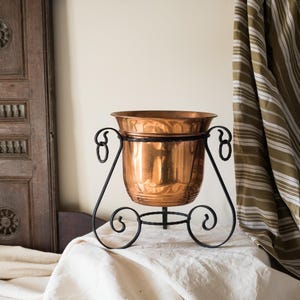 May include: A white ceramic mug with a black handle and the text "But First, Coffee" in a bold, black font. The mug is set against a blurred background, suggesting a cozy setting. The mug appears to be approximately 4 inches tall.