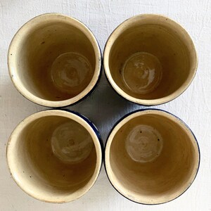 May include: Four ceramic cups with a blue rim and a white interior. The cups are arranged in a square pattern.