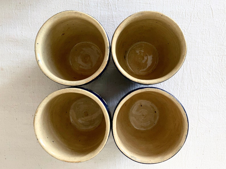 May include: Four ceramic cups with a blue rim and a white interior. The cups are arranged in a square pattern.