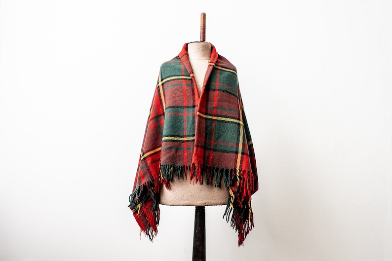 May include: A red, green and yellow plaid wool shawl with fringe on the edges. The shawl is draped over a mannequin.