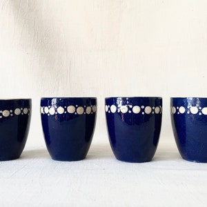 May include: Four blue ceramic egg cups with a white dotted design around the top edge.