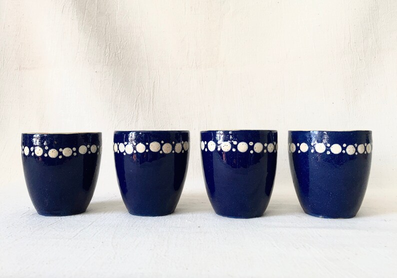 May include: Four blue ceramic egg cups with a white dotted design around the top edge.