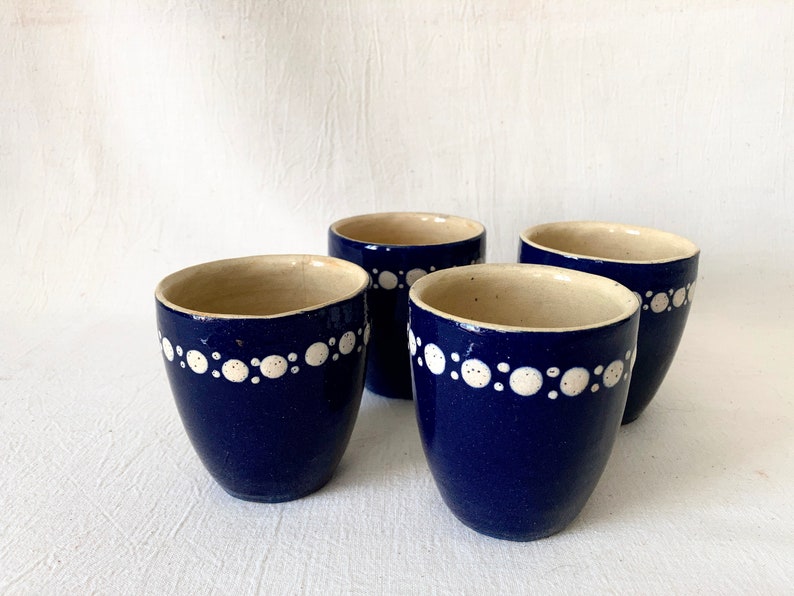 May include: Four blue ceramic mugs with white polka dot designs around the rim.