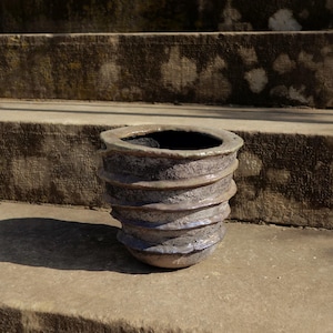 May include: A gray ceramic planter with a textured, ribbed design. The planter is empty and sits on a set of stone steps.