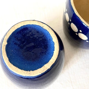 May include: Two blue ceramic mugs with white polka dots. The mugs are empty and have a glazed finish.