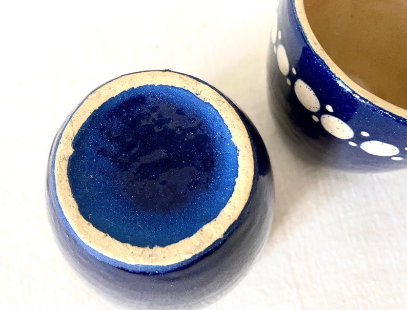 May include: Two blue ceramic mugs with white polka dots. The mugs are empty and have a glazed finish.