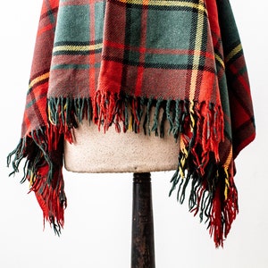 May include: A red, green and yellow plaid throw blanket with fringe on the edges. The blanket is draped over a mannequin.