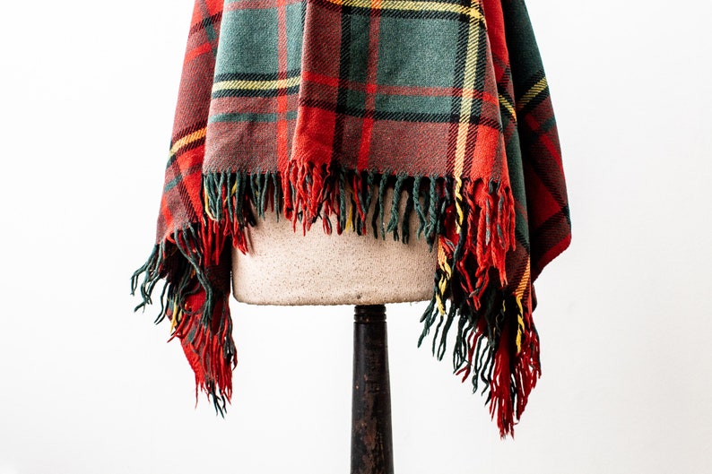 May include: A red, green and yellow plaid throw blanket with fringe on the edges. The blanket is draped over a mannequin.