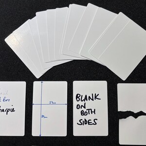 May include: A collection of white rectangular cards with rounded corners. One card shows the text Pencil, Ink Biro, and Sharpie. Another card displays dimensions of 57mm by 89mm. A third card reads BLANK ON BOTH SIDES. One card is torn in half.