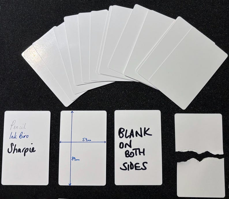May include: A collection of white rectangular cards with rounded corners. One card shows the text Pencil, Ink Biro, and Sharpie. Another card displays dimensions of 57mm by 89mm. A third card reads BLANK ON BOTH SIDES. One card is torn in half.