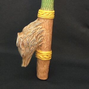 May include: A wooden pipe with a wolf head at the bottom. The pipe is decorated with yellow, green, and red bands. The wolf head is carved in detail and has a realistic appearance.