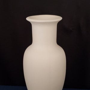 May include: A tall, off-white vase with a rounded body and a flared rim. The vase has a smooth, matte finish and stands on a dark blue surface against a black background. The vase's height is approximately 12 inches.