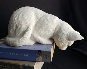 May include: White ceramic cat figurine with a sleeping pose, resting on top of two books. The books are titled "The Count of Monte Cristo" and "Little Women".