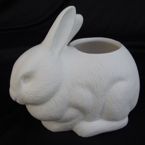 May include: White ceramic planter shaped like a rabbit, with a round opening for planting. The rabbit is sitting with its head down and its ears are upright.