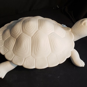 May include: A white ceramic turtle figurine with a detailed shell pattern. The turtle has its head and four legs extended, and is set against a black background. The figurine is a decorative item.