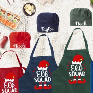 May include: Set of four personalized chef hats and aprons with the names Taylor, Noah, Nicole, and William. The aprons are blue, green, and red with the text "Elf Squad" and a cartoon elf graphic.