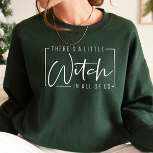 May include: A dark green sweatshirt with the text "There's a little Witch in all of us" printed on the front.