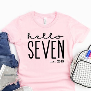 Peut inclure: T-shirt rose avec un texte noir qui dit "hello seven est. 2015".