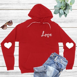 Peut inclure: Sweat-shirt à capuche rouge avec des cœurs blancs sur les manches et le mot "Love" sur le devant.