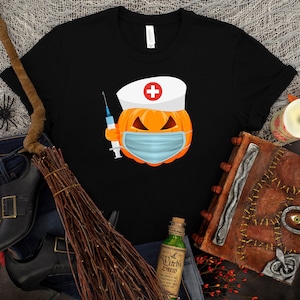 May include: Black t-shirt with a graphic of a pumpkin wearing a nurse's hat and a face mask, holding a syringe. The pumpkin has a scary expression.