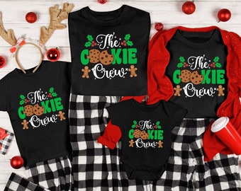 May include: A family matching set of black pajamas with a white graphic print of a gingerbread cookie and the text "The Cookie Crew". The pajamas are in a black and white plaid pattern.