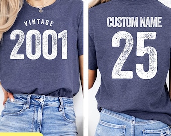 May include: Navy blue t-shirt with the text "VINTAGE 2001" on the front. The back of the shirt has the text "CUSTOM NAME" above the number "25". The shirt is a crew neck style and is made of a soft material.
