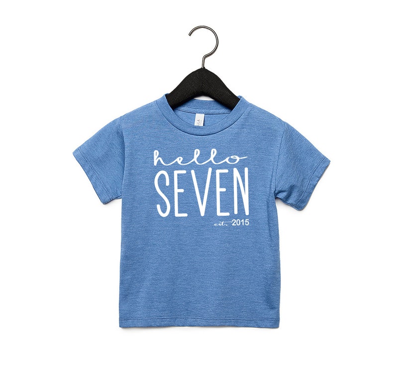 Peut inclure: Un t-shirt bleu &agrave; manches courtes avec du texte blanc qui dit "hello seven est. 2015".