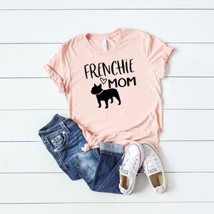 May include: Pink t-shirt with a black silhouette of a French Bulldog and the text "Frenchie Mom" with a small heart.