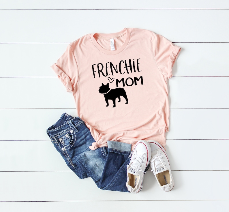 May include: Pink t-shirt with a black silhouette of a French Bulldog and the text "Frenchie Mom" with a small heart.