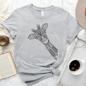 May include: A gray t-shirt with a black and white patterned giraffe design. The giraffe's head is peeking out from the left side of the shirt.