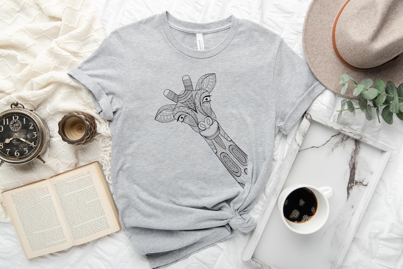 May include: A gray t-shirt with a black and white patterned giraffe design. The giraffe's head is peeking out from the left side of the shirt.