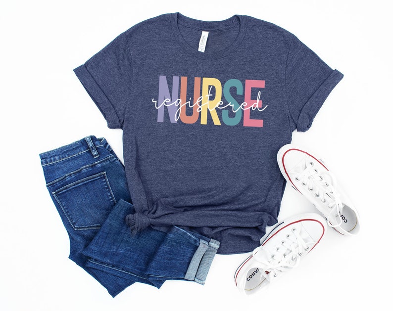 Pu&ograve; includere: Una maglietta blu navy con il testo "NURSE registered" in colori arcobaleno. La maglietta &egrave; abbinata a jeans blu e scarpe da ginnastica bianche.