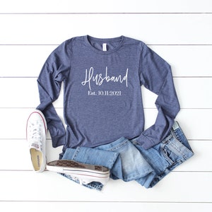 Puede incluir: Una camiseta de manga larga azul marino con el texto "Husband Est. 10.11.2021" en letras blancas.