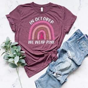 May include: A maroon t-shirt with a pink glitter rainbow and the text "In October We Wear Pink".