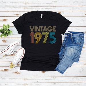 May include: Black t-shirt with the text "Vintage 1975" in rainbow colors. The text is in a retro font style.