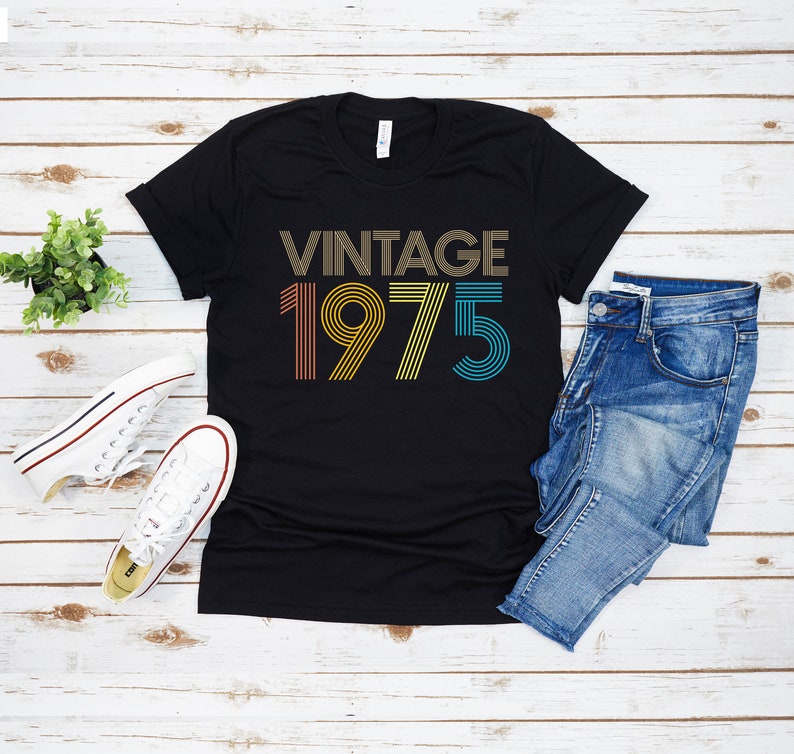 May include: Black t-shirt with the text "Vintage 1975" in rainbow colors. The text is in a retro font style.
