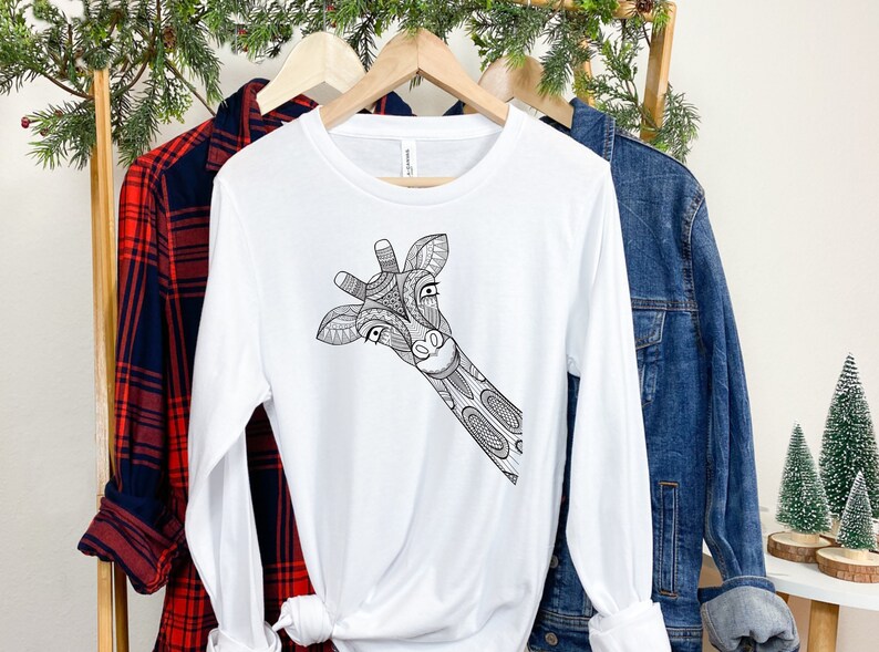 May include: White long-sleeve t-shirt with a black and white illustration of a giraffe's head peeking out from the side.