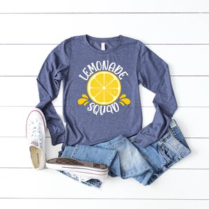 May include: A navy blue long-sleeved shirt with a white graphic of a lemon and the text "Lemonade Squad".