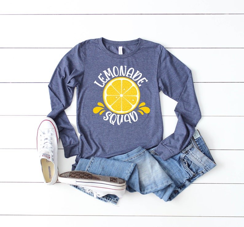 May include: A navy blue long-sleeved shirt with a white graphic of a lemon and the text "Lemonade Squad".