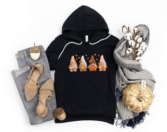 May include: Black hoodie with a graphic of four gnomes holding pumpkins and surrounded by falling leaves. The gnomes are wearing brown, orange, and red hats.