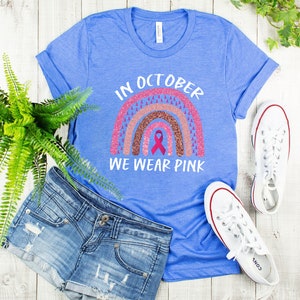 May include: A blue t-shirt with a pink and brown glitter rainbow design and the text "In October We Wear Pink".