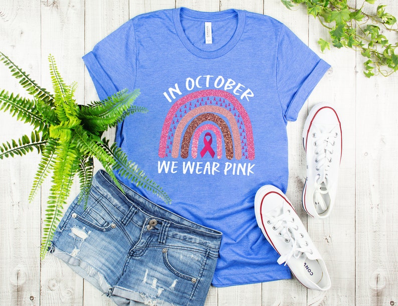 May include: A blue t-shirt with a pink and brown glitter rainbow design and the text "In October We Wear Pink".